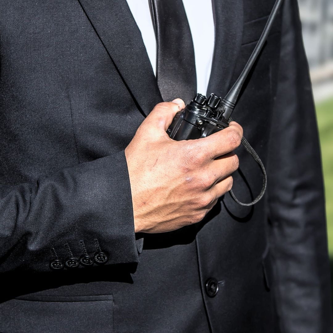 Professional close protection officer in a dark suit communicating via walkie-talkie during a secure transfer.
